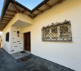 white exterior, wooden door, black metal window grill, black roof, stone pathway