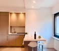 modern kitchen with white countertops, wooden cabinets, white chairs, wine bottle, wine glasses, flowers, radiator, window