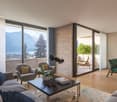 modern living room with large windows, balcony, wooden floor, couch, coffee table, armchairs, dining table, chairs, plants, lamp