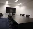 empty conference room with a large table, black chairs, a flat screen TV, and white walls