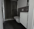 Bathroom with shower, two toilets, white cabinets, black floor