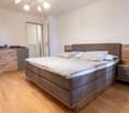 large bed, wooden bedside tables, wooden floor, white walls, cabinet with drawers