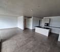Empty room with white walls, gray tiled floor, kitchen island with black countertop, white cabinets, and a sink with a faucet.