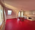 Red floor, large windows, kitchen with countertop, cabinets, sink, oven, central heating
