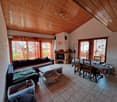 Spacious living room with vaulted wood ceiling, large windows, fireplace, sofa, coffee table, and dining area with table and chairs