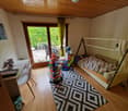 Bedroom with wooden ceiling, large windows overlooking a balcony or terrace, bed, desk, and various toys and decorations