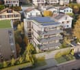 apartment building with several floors, solar panels on the roof, balconies on some floors, surrounding houses and greenery