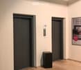 The image shows a hallway with two elevator doors, a wooden floor, and a black box-like object on the floor.
