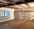 large wooden beam ceiling, hardwood floors, stone wall, single window with a white radiator