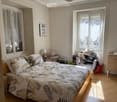 Double bed, bed sheets with leaf pattern, lamp, white cabinet, chair with pile of clothes, basket, picture frame