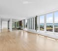 Spacious open-plan living area with large windows offering a scenic view, hardwood flooring, and a modern, minimalist design.