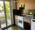kitchen with a sliding door to the balcony, green tiles, white appliances, wooden cabinets, gas stove, oven, sink, power outlet