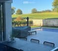 Outdoor dining table, chairs, umbrella, pool, stone wall, trees, grassy field