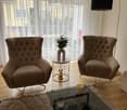 brown armchairs, coffee table, side table with vase, floor lamp, window with white curtains
