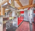 open kitchen, stainless steel countertops, red cabinets, refrigerator, microwave, stove, stainless steel hood, log ceiling, carpeted floor, trash can
