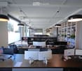 Large office space, several rows of desks with computers, cabinets, monitors, shelves with books and files, pendant lights.