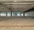 Empty, industrial-style space with exposed beams, concrete floor, and glass windows.