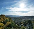 cityscape, mountains in the background, trees in the foreground, blue sky with clouds
