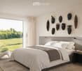 modern styled bedroom with gray walls, wooden floor, glass wall with view of grassy field, gray bed, white and gray bedspread, night tables with lamps, decorative masks on the wall