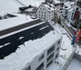 White building with balconies, solar panels on the roof covered in snow, surrounded by snow-covered landscape