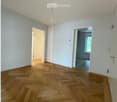Empty room with wooden parquet flooring, white walls, and two doors leading to other rooms.