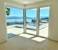 modern interior, large glass sliding doors, wooden flooring, balcony overlooking the sea, scenic mountains in the distance
