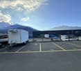 Empty parking lot with yellow lines, mountains in the background, a white trailer with a boat, and a building with a ladder.