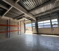 Empty garage with concrete floor, metal shelving units, large garage doors, and natural light from windows.