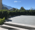 Raised ground floor, paved area, bushes, mountains in the background