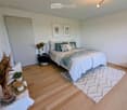 Bedroom with bed, rug, nightstand, plants, and framed pictures on the wall