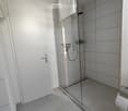 Modern bathroom with glass shower enclosure, white tiles, white door, towel rack, and toilet paper holder.