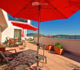 Terrace with lounge chairs, tables, chairs, and umbrellas, with a view of the city