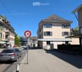 Urban street with a speed limit sign, buildings, parked cars, and pedestrians.
