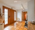 Corridor / Hallway. A well-lit hallway with tiled flooring, wooden doors, a coat rack with jackets, a small wooden chair, and decorative items including hats and a vase with dried plants.