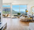 Furnished Room. Bright living room with large windows offering a scenic mountain view, featuring a white sofa, a round table with chairs, a floor lamp, a television, and a bookshelf.