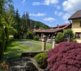 A well-maintained garden with a variety of plants, flowers, and trees, featuring a stone pathway, a bench, and a small pond with rocks and aquatic plants.