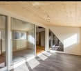 Bright, minimalist room with wooden ceiling, large glass walls, and natural light. The space is empty, with no furniture or furnishings visible.