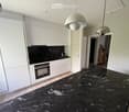Modern kitchen with white cabinets, black marble countertops, and built-in oven. Pendant lights hang above the island.