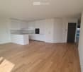 Empty kitchen with white cabinets, wooden flooring, and a black door leading to another room.