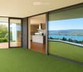 Bright, modern room with green carpeting, large glass sliding doors opening to a balcony, and a visible kitchen area with white cabinets and stainless steel appliances.