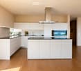 Modern kitchen with white cabinets, a central island, black countertops, and built-in appliances including an oven and range hood. The space features wooden flooring and a small potted plant on the counter.