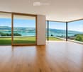Empty room with wooden flooring, large glass sliding doors, and scenic view of a lake and landscape.
