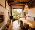 Cozy dining area with a large wooden table, chairs with fur cushions, a stone fireplace, and a chandelier hanging from the wooden ceiling.