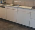 Modern kitchen with white cabinets, stainless steel sink, and dishwasher. Grey tiled backsplash and dark grey concrete-style flooring.