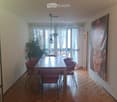 Dining room with wooden parquet flooring, a large wooden dining table surrounded by red chairs, a large painting on the wall, and a potted plant near the window.