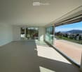 Empty room with large glass sliding doors leading to a balcony, offering a scenic view of the landscape and city.