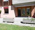Two-story residential building with a modern facade, large glass doors, and a well-maintained garden area with stone planters and a paved walkway.