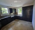 Empty kitchen with dark wooden cabinets, a tiled floor, and two windows letting in natural light.