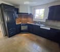 Modern kitchen with dark cabinets, granite countertops, a stainless steel sink, and a refrigerator. The floor is tiled in a herringbone pattern.