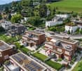 Aerial view of a residential area with modern houses, solar panels on rooftops, well-maintained gardens, and a scenic green landscape in the background.